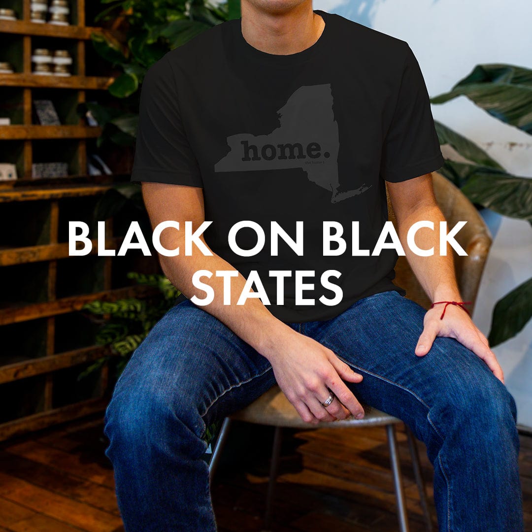 Man wearing The Home T black-on-black state pride T-shirt in a cozy interior setting